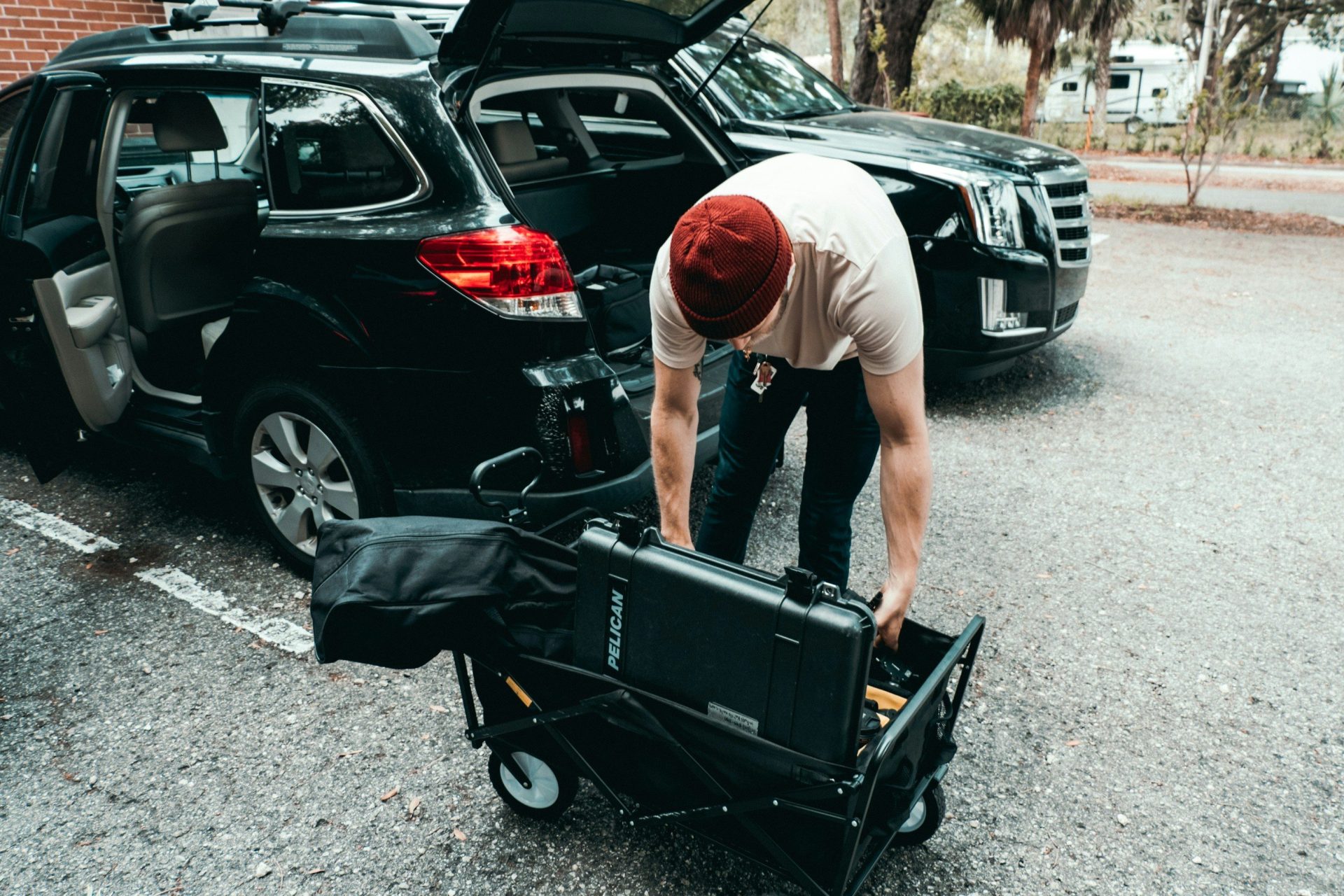 Mann im grauen T-Shirt und mit schwarzer Shorts hält tagsüber einen schwarzen Kinderwagen neben einem schwarzen SUV.